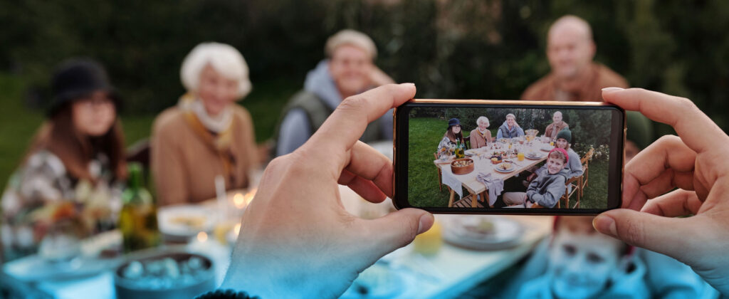 Multi-generational family gathered around a table with someone taking a photograph with a phone